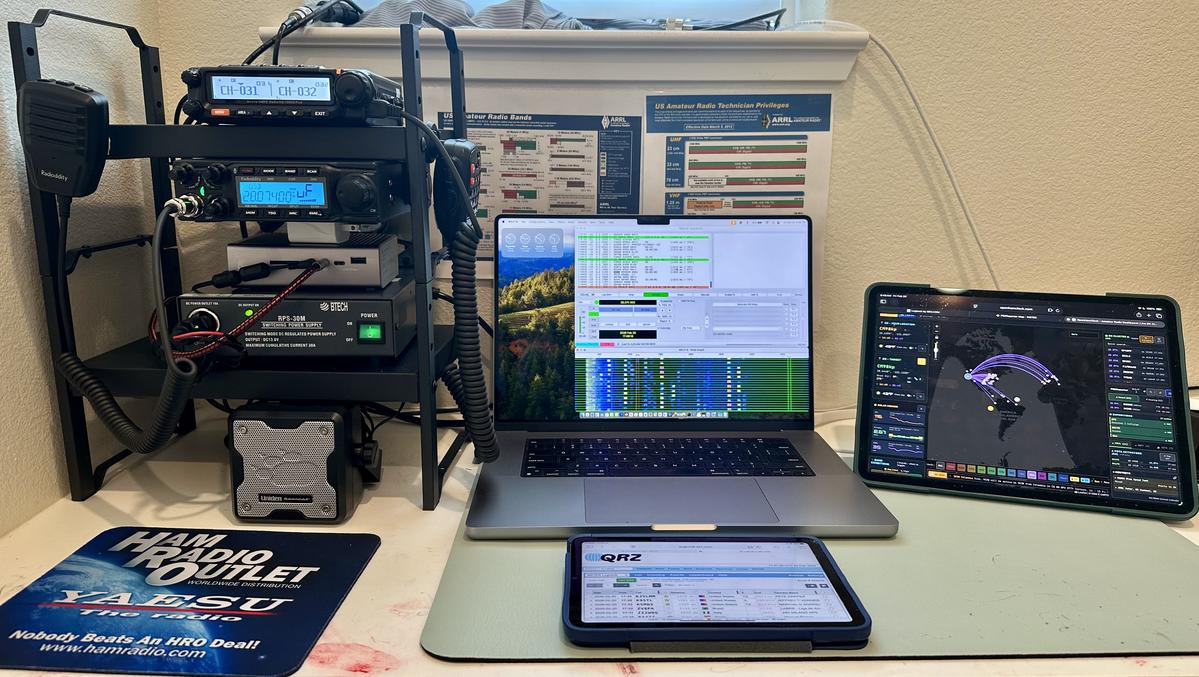 Dan's radio desk with a Radioddity radio, microphones, laptop running digital radio software, and a tablet displaying a contact map.